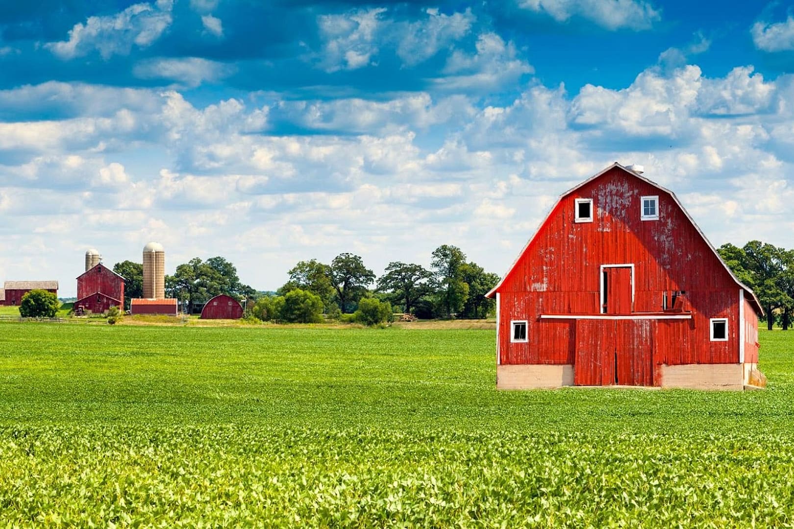 Red Barn with a cloudy and sunshining sky behind it, lush green field in the foreground
