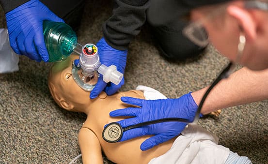EMS workers provide oxygen to a pediatric manikin during a training exercise