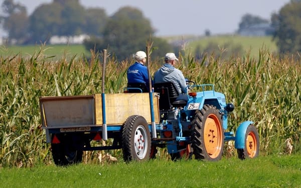 tractor-6608040_1280 Two men sit on a tractor with a field of corn behind them